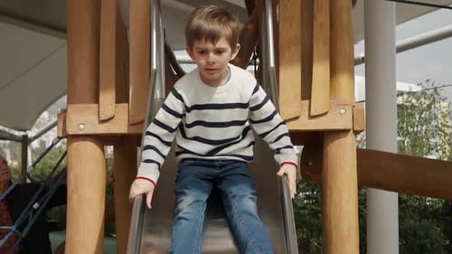 Extreme slow motion of cheerful boy riding down the wooden slide on outdoor playground at park