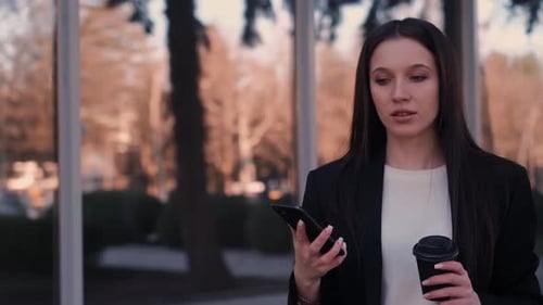 Young Woman Using Phone While Holding Coffee