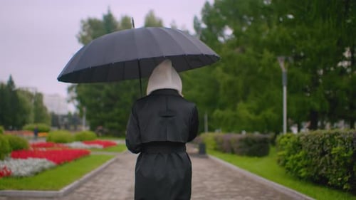 Back Shot of Woman in Black Coat with Hood Holds Umbrella While Walking