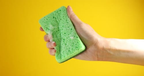 Woman squeezing sponge with foam on orange background, closeup