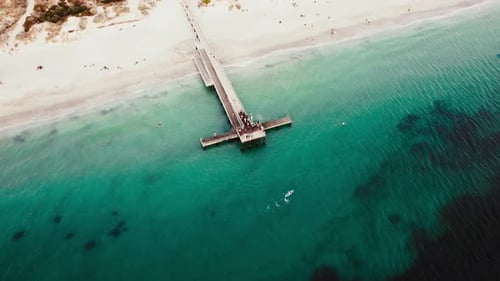 Aerial view of a coastal pier extending into turquoise water with beachgoers