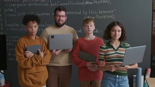 Porträt eines Programmierlehrers und seiner Schüler mit Geräten vor Blackboard