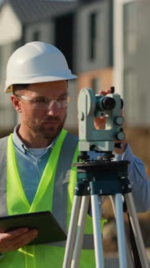 Man Using Theodolite and Holding Tablet on Construction Site