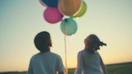 Two Children Holding Hands and Balloons in Field