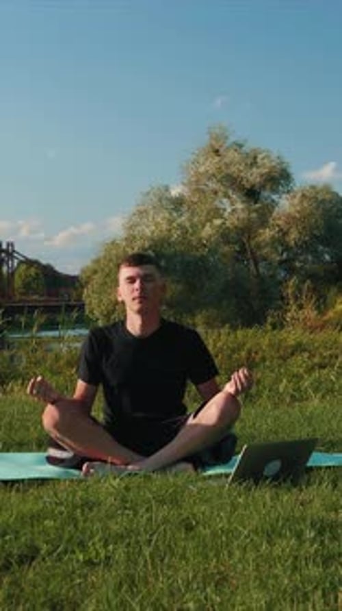 Man Meditating Outdoors with Laptop in Peaceful Field