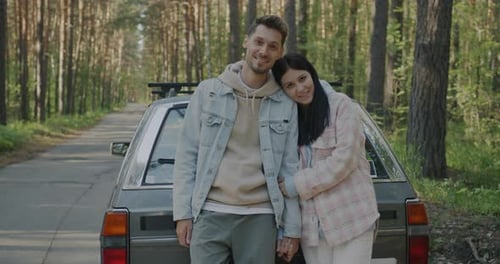 Happy Couple Standing Outdoors in Forest Next to Automobile Relaxing From Road Trip in Countryside