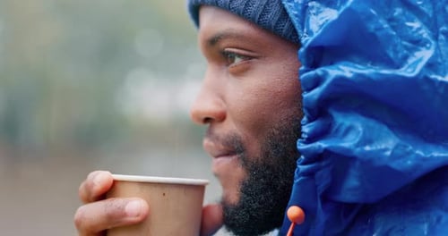 Man in Rain Jacket Drinks Coffee Outdoors
