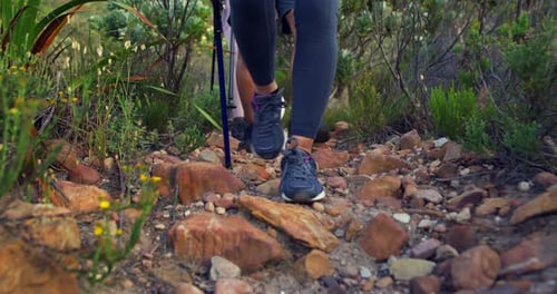 Closeup of hikers walking on stones down a rocky trail on a mountain with hiking sticks