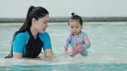 happy mother with toddler baby girl in a swimming pool