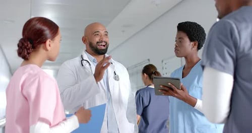 Diverse doctors discussing work and using tablet in corridor at hospital, slow motion