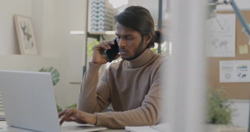 Portrait of Indian Manager Working with Laptop and Speaking on Mobile Phone in Office