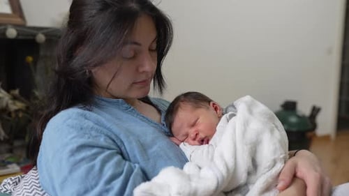 Mother Holding Newborn Baby in Her Arms Indoors