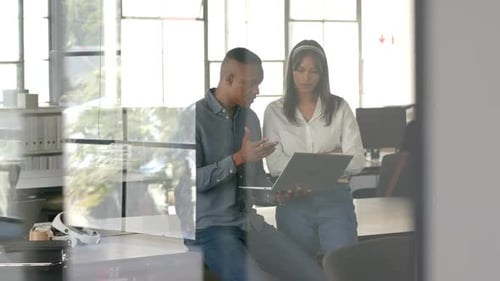 Discussing project details, colleagues using laptop in modern office setting