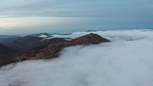 Majestic mountains peaking through a serene sea of clouds at dusk, evoking tranquility, aerial view