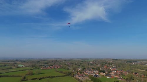 Aerial video high above the village as a paraglider soars peacefully across a wide open sky.