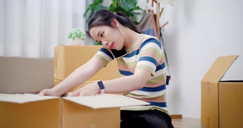 Woman Packing Boxes and Talking on Smartphone