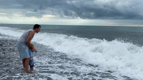 Caring Father and Son Playing with Sea Waves Father Lifts Son When Wave is Approaching