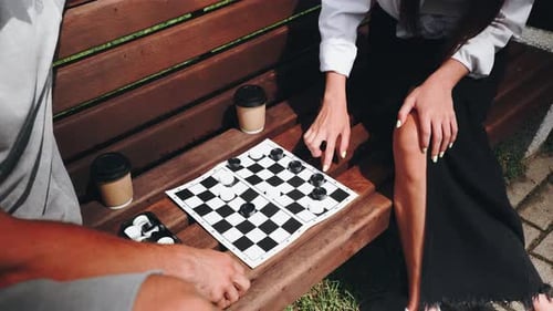 A Couple Enjoys a Game of Checkers on a Park Bench Surrounded By Greenery Sipping Coffee and
