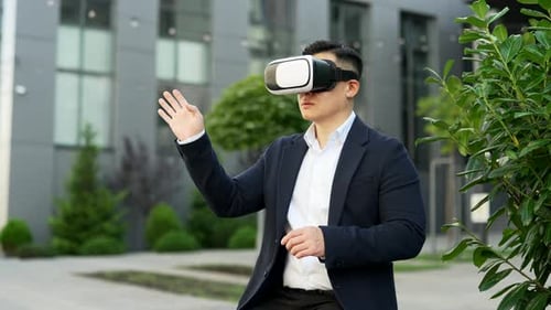 Asian businessman works using VR glasses in virtual reality simulator sitting on a bench on street