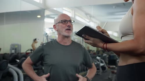Adult Man Talking to Female Coach about Training Plan in Gym