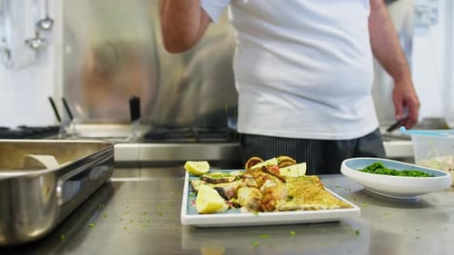 Chef Adds Chopped Parsley To A Second Fish Dish At Restaurant Kitchen