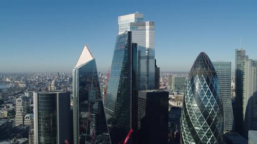 Descending Aerial shot of the London financial district's iconic skyscrapers under a clear blue sky.
