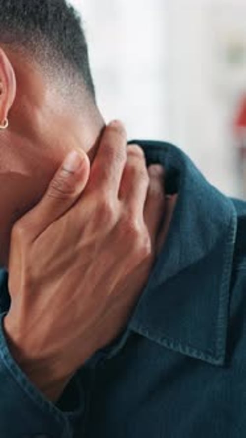 Young Man Rubs His Neck Indoors