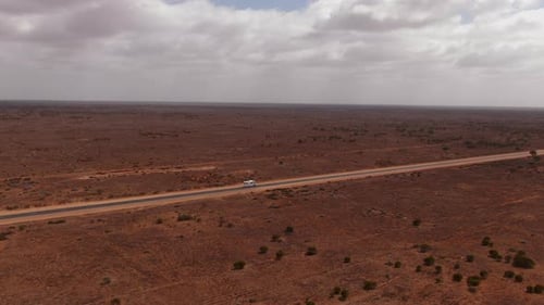 Aerial view of white camper van on empty highway surrounded by red desert in Australia during cloudy