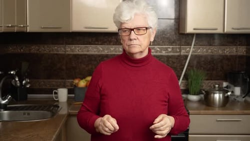 Senior Woman Putting on Eyeglasses in Kitchen