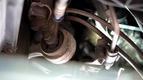 Mechanic in his garage shop looking underneath a car or industrial equipment with flashlight torch,
