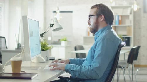 Close-up of a Young Bearded Man Working on Personal Computer in His Light and Modern Office.
