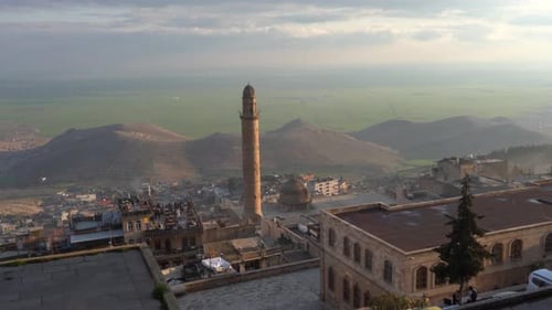 The camera zooms in towards the Mardin Ulu Mosque. Behind the cut stone mosque, the unique view of M