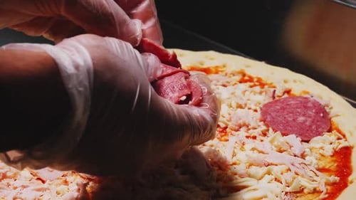 Chef Puts Sausage Slices Onto Raw Pizza on Table in Cafe