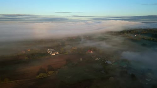 An aerial view of the countryside with picturesque houses shrouded in the morning mist.