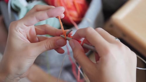 Hands Knitting Orange Yarn with Knitting Needles