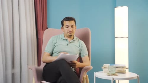 Young Man Writing on Paper in Chair Indoors