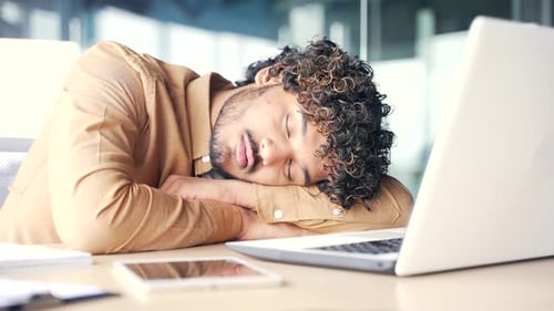 Young overworked employee sleeping at office desk at workplace with laptop startup finance job. Lazy
