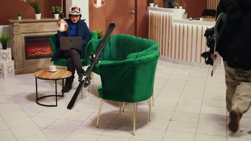 Woman with skis using laptop in hotel lobby