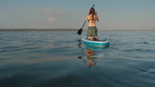 Woman Paddleboarding on Water Kneeling on Board