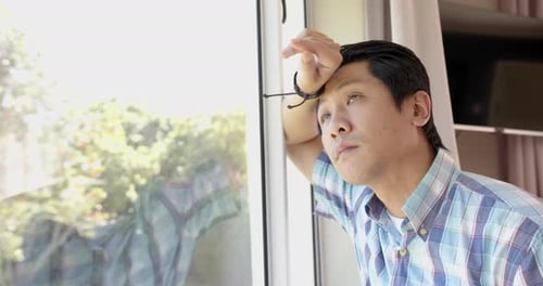 Thoughtful Young Man Resting Head Against Window Frame