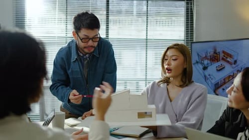 Architects and designers work presenting and discussing house model in office meeting.