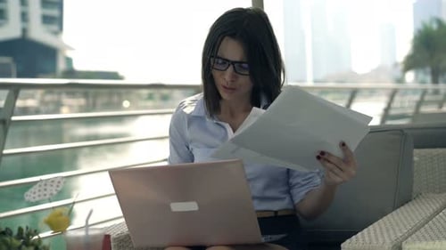 Young Businesswoman Working with Laptop and Documents in Cafe in City 30s