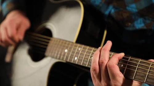 Hands of young man practicing on acoustic guitar strings learning new chords on a music course