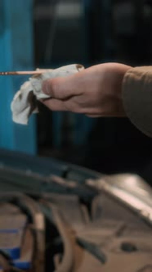 Hands of Specialist Using Dipstick to Examine Engine Oil Level of Auto