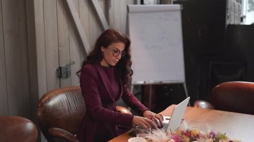 A Professional Woman Engaged in Work on Laptop Within a Modern Office Environment Setting