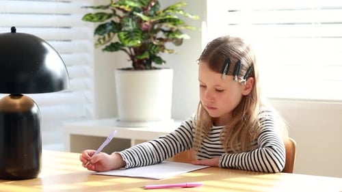 La linda niña escribe con cuidado y atención en Home at the Table Educación primaria