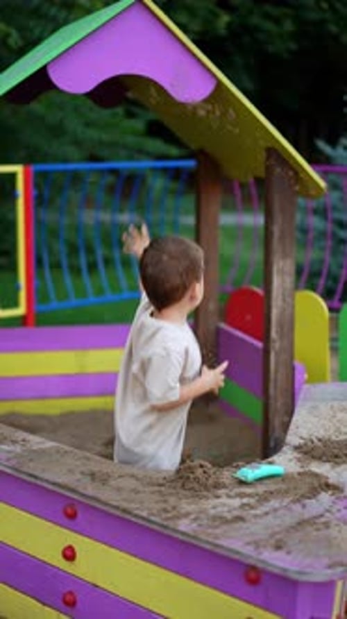 Enfant caucasien jouant dans le bac à sable. Enfant joyeux jetant du sable sur les côtés. Vidéo verticale.