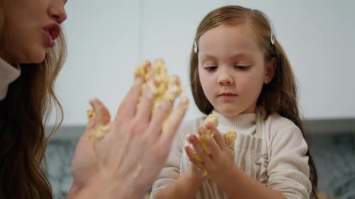 Mother and daughter hands rolling dough together at home in modern kitchen