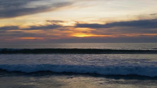 4K Drone footage of sunset over the ocean with waves and clouds.