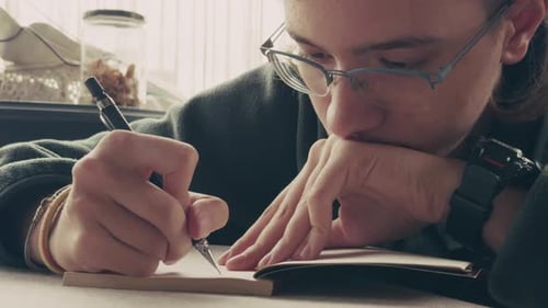 Young Adult Writing in Notebook with a Pen